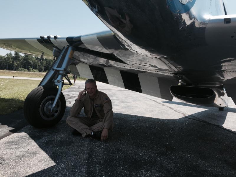 Texas Flying Legends Museum pilot Mark Murphy takes a phone call under the wing of a World War II, P-51 Mustang shortly after landing it at Wiscasset Municipal Airport on July 28. SUSAN JOHNS/Wiscasset Newspaper Texas Flying Legends, Mark Murphy