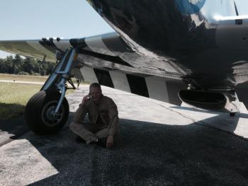 Texas Flying Legends Museum pilot Mark Murphy takes a phone call under the wing of a World War II, P-51 Mustang shortly after landing it at Wiscasset Municipal Airport on July 28. SUSAN JOHNS/Wiscasset Newspaper Texas Flying Legends, Mark Murphy