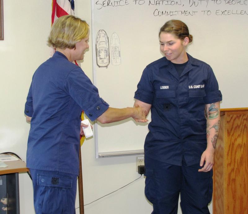 CG Rear Admiral Fagan presents a US Coast Guard First District challenge coin to Seaman Julienne Loeber in recognition of her outstanding contributions to the Boothbay Harbor community. In addition to her regular duties at the station, Loeber is active in numerous local charities and organizations in the Boothbay area including Habitat for Humanity, the food bank and CG Station Boothbay Harbor’s Thanksgiving and Christmas Families. The tradition of the challenge coin goes back to World War I, and has evolved into a symbol of recognition and camaraderie in military units; the coin is always presented in a handshake and is never handed out as would be a token or souvenir. Courtesy of Ted Chatham/USCG Auxiliary