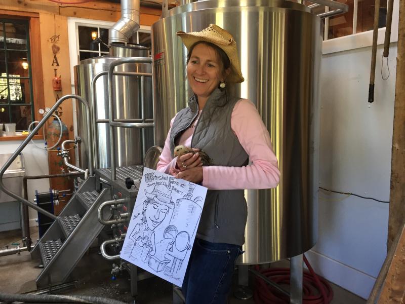 Co-owner of the Boothbay Craft Brewery, Lori Mitchell, poses with a baby Gypsy chicken and caricature drawn by Leona Hosack at the Boothbay Craft Brewery's “Declaration of Fermentation.” KATRINA CLARK/Boothbay Register