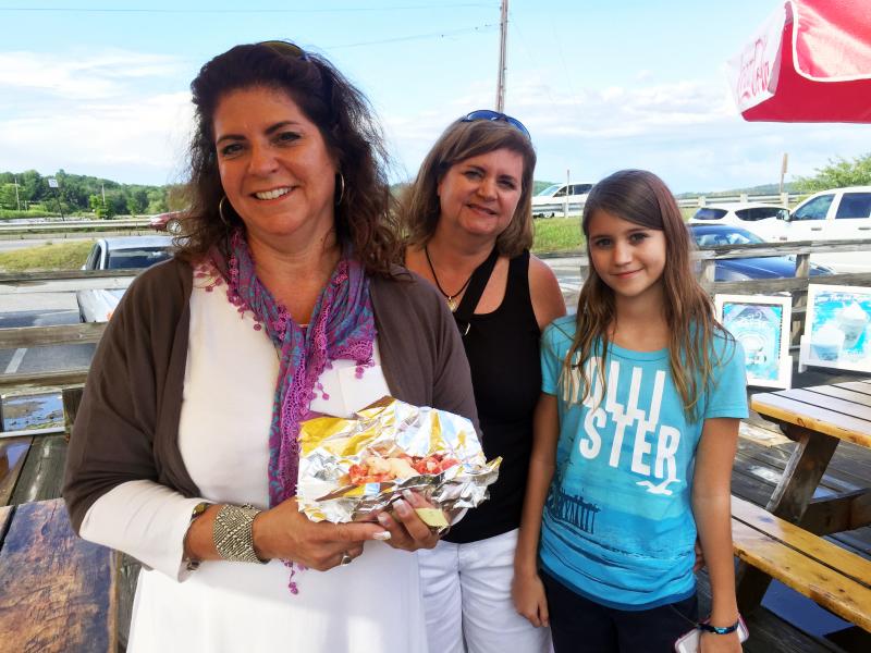 Karen Johnson, left, from Cincinnati, Ohio, shows off her lobster roll at Sprague’s Lobster, while Laurie Pitosh and daughter Kate, from Orlando Florida, stand by. SUZI THAYER/Boothbay Register
