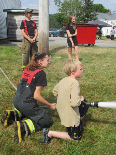 Woolwich junior firefighter Lilly Maccio gives some advice to Gage Barnes on how to handle a fire hose. Josh Demers and Sydney McCaren look on. PHIL DI VECE/Wiscasset Newspaper