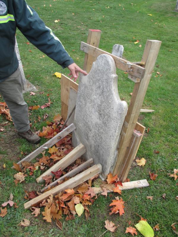 Christiansen shows how a temporary brace is used to support a gravestone until the epoxy holding it together hardens. PHIL DI VECE/Wiscasset Newspaper