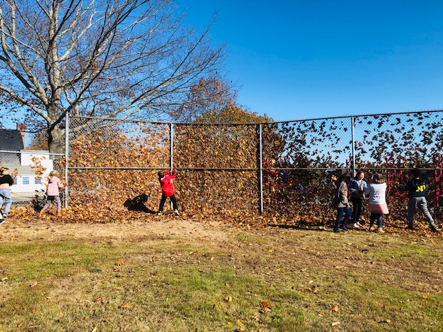 Students throw leaves as the wind makes a wall against the ball field fence on a sunny, windy afternoon. Cindy Collamore photo
