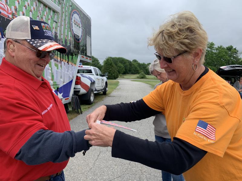 Wreaths Across America volunteer Richard Barter gets a bracelet from Wiscasset Speedway co-owner Vanessa Jordan July 3 as Wreaths sets up its mobile education display. SUSAN JOHNS/Wiscasset Newspaper