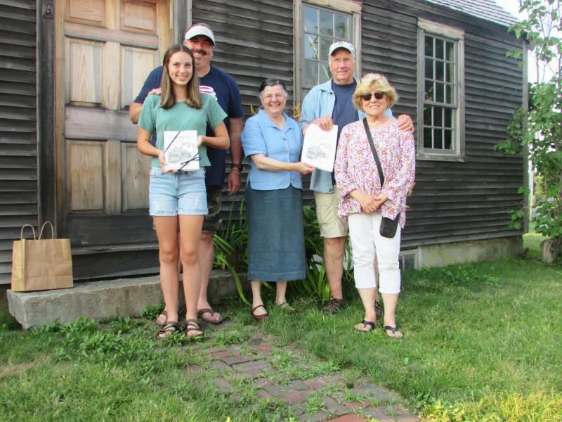 Louise Miller, of the Chapman-Hall House Stewardship Committee, presents Sandi and Dan Day, their son Justin, and his daughter Zofie, with towels printed with Maurice “Jake” Day’s drawing of the Chapman-Hall House. Sons, Matthew and Darryl Day were not available for the photo. Photo taken in front of Chapman-Hall House. Courtesy of LCHA
