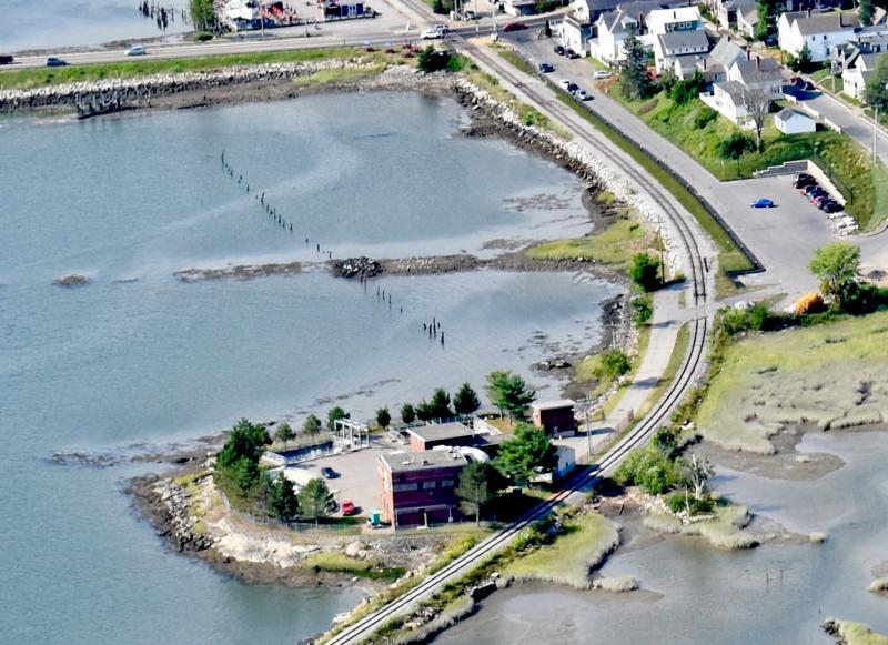 Cow Island as it now looks showing Wiscasset’s sewer treatment plant, railroad tracks and causeway. The rows of piling in the river show the path of the former Wiscasset, Waterville and Farmington Railroad, a narrow gauge railway that operated from 1895 until 1933. At the top, U.S. Route 1 leads motorists over Donald E. Davey Bridge and, at the right, is Railroad Avenue where the former train station was until it was moved to North Edgecomb in the 1980s. PHIL DI VECE/Wiscasset Newspaper