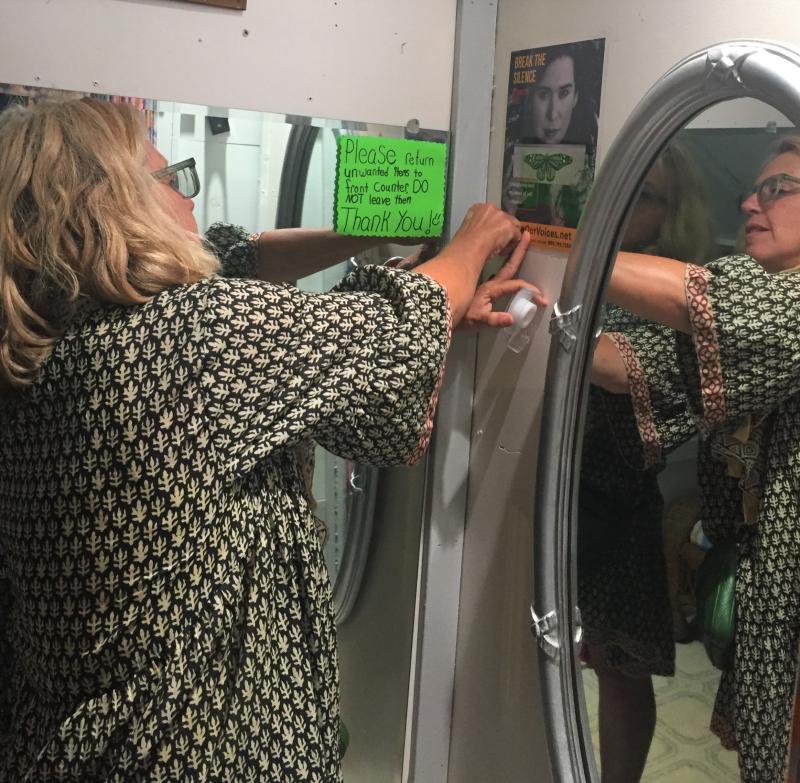 Patrisha McLean fastens a Finding Our Voices poster in the dressing room of Gretchen’s Closet. LISA KRISTOFF/Boothbay Register