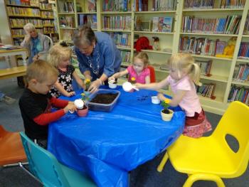 Children's Librarian Judy Flanagan assists in potting the plants at Story Time this past week. The children then gave the potted flowers to the mothers or grandmothers who bring the children to Story Time each week. Courtesy of Wiscasset Public Library