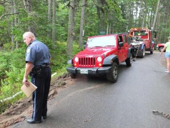 A Jeep Wrangler mail truck is towed out of Appalachee Pond in Boothbay Harbor, as Officer Richard Mirabile examines the accident scene on July 9. RYAN LEIGHTON/Boothbay Register
