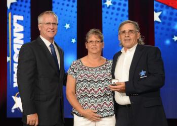 Landstar President and CEO Jim Gattoni, left, presents Woolwich’s Joe Westleigh with an award at Landstar’s All-Star Celebration in Nashville, Tennessee. Westleigh’s wife Melisa joins in the ceremony on-stage. Courtesy of Landstar System