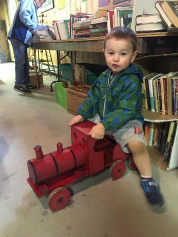Liam Aarons, 2, of Woolwich rides a toy train while his mother helps with a yard sale-fundraiser. SUSAN JOHNS/Wiscasset Newspaper