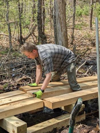 Coastal Rivers Lands and Stewardship Coordinator Gunnar Nurme moves boards into place during construction of the new bog bridge. Courtesy of Coastal Rivers