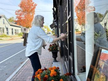Surrounded by the fiery colors and reflections of the season, Ann Scanlan arrives at her Sylvan Gallery on Water Street, Wiscasset Friday morning, Oct. 2. SUSAN JOHNS/Wiscasset Newspaper 