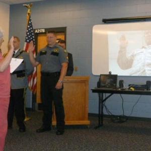 Jail Authority Clerk Katharine Martin-Savage swears in newly promoted officers at the Promotion Ceremony held at the Two Bridges Regional Jail. Sergeant Richard Wardwell, seen on the projection screen on the right, participated in the ceremony through Skype from Abu Dhabi in the United Arab Emirates where he is currently deployed as a member of the National Guard. Photo Courtesy of Two Bridges Regional Jail