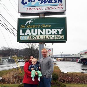 Terri and Darick Herald, with their 16-month-old daughter, Charlotte, stand in front of the signs of their new businesses, Coastal Car Wash and Harbor’s Choice Laundry. SUZI THAYER/Boothbay Register