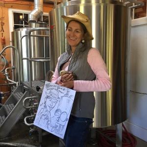 Co-owner of the Boothbay Craft Brewery, Lori Mitchell, poses with a baby Gypsy chicken and caricature drawn by Leona Hosack at the Boothbay Craft Brewery's “Declaration of Fermentation.” KATRINA CLARK/Boothbay Register