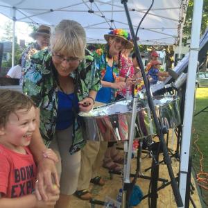 Hunter Rogers, 3, of Woolwich plays as Nina Andersen and other Pan Fried Steel members look on, at the July 12 installment of the "Alive on the Common" concert series in Wiscasset. SUSAN JOHNS/Wiscasset Newspaper
