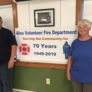 Alna Fire Chief Mike Trask and his mother and fellow member Coleen Trask with the 70th anniversary banner June 12. SUSAN JOHNS/Wiscasset Newspaper