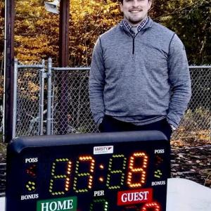 WMHS Athletic Director Cameron Bishop stands below the old scoreboard. This past soccer season, the school relied on the temporary scoreboard shown here on the table. PHIL DI VECE/Wiscasset Newspaper