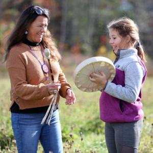 Passamaquoddy educator Sandra Bassett invites a student from Jefferson Village School to try out a traditional drum. Courtesy of Coastal Rivers
